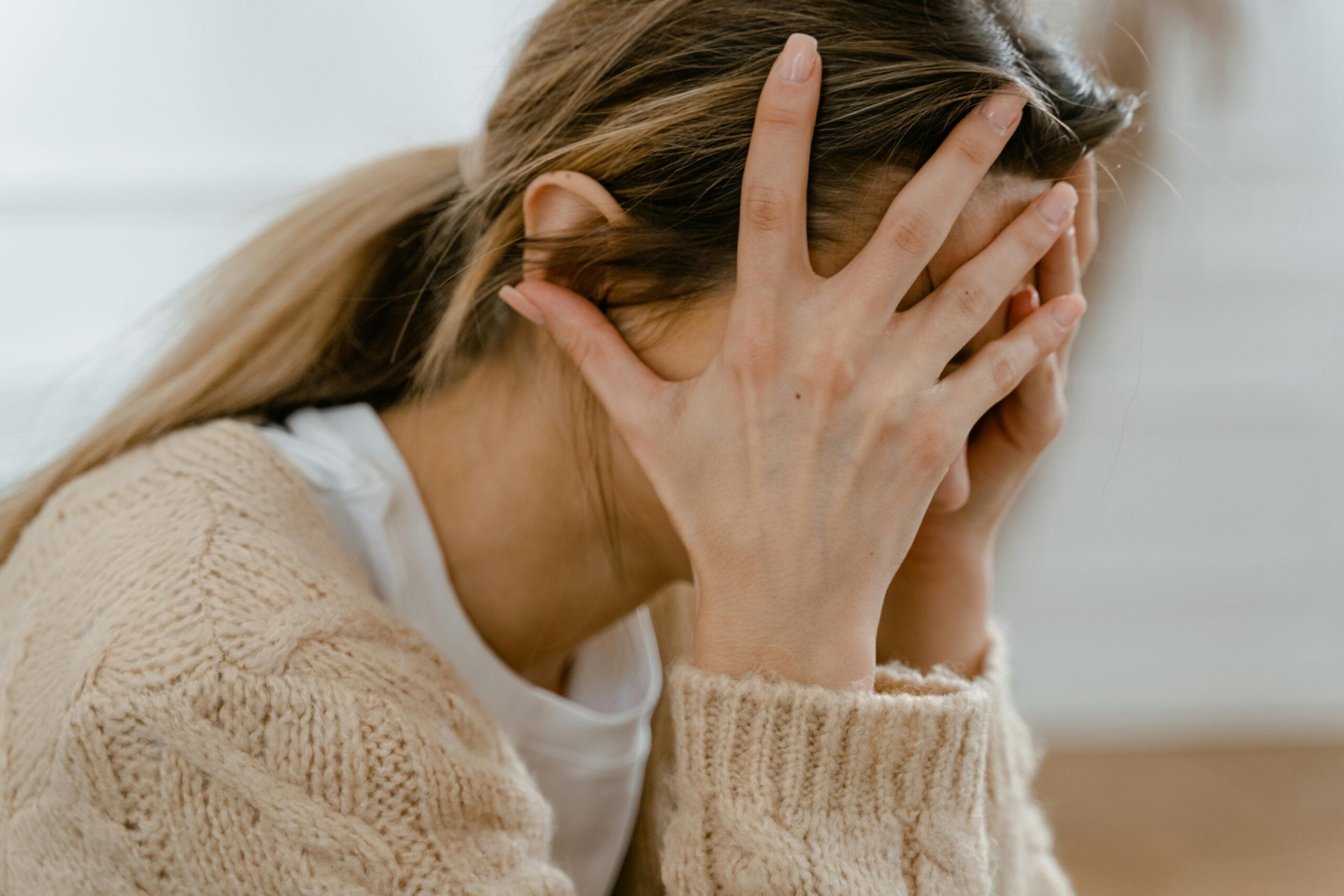 Stressed woman with hands covering her face, symbolizing emotional struggle and a victim mindset