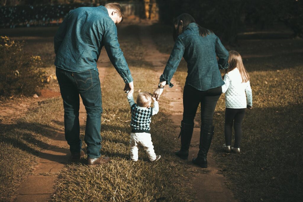 Parents guiding their toddler on a sunny outdoor path, symbolizing growth and overcoming a victim mindset through supportive parenting